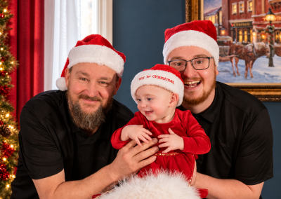 Baby, Grandpa, and dad giggle in front of Christmas tree at Drummond Manor in Waterdown On