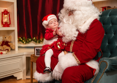 Santa holding a sleepy baby in a teal armchair during a Christmas portrait session at Drummond Manor
