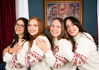 Four women in matching Christmas sweaters posing beside a decorated tree at Drummond Manor in Waterdown