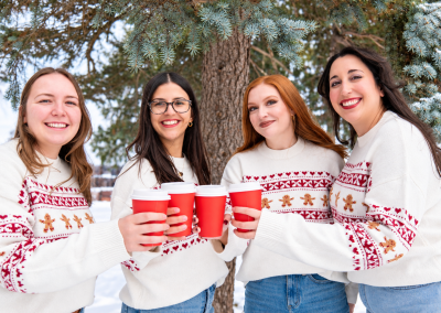 Four friends wearing matching holiday sweaters and holding red coffee cups outdoors in winter